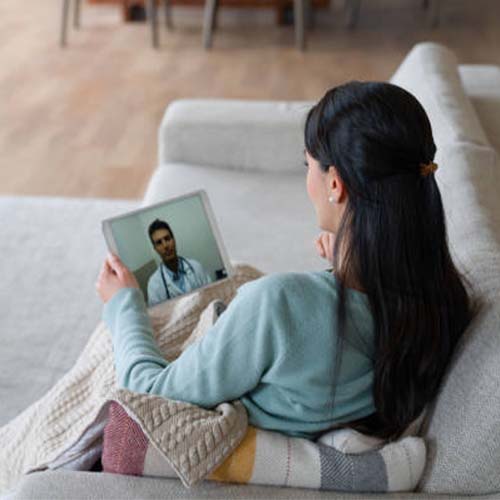 woman with long brown hair in blue shirt holding laptop using video by Allied Healers